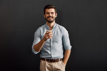 Fresh espresso. Cheerful young bearded man holding a cup of hot coffee and looking at camera with...