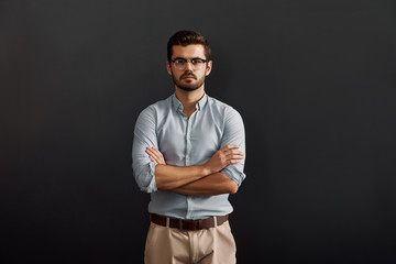 Fototapeta na wymiar Portrait of confidence. Serious young bearded man looking at camera and keeping arms crossed while standing against dark background