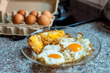 Fried eggs in a glass pan with fresh raw eggs in background.