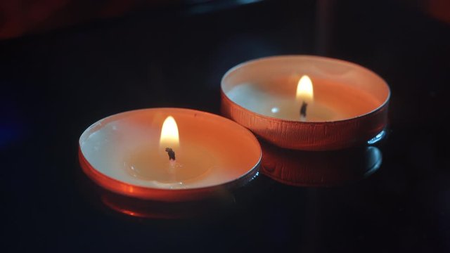 Two small candles floating in the water in the darkness illuminated with warm tones, close up
