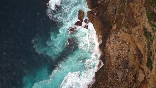 Ocean waves crashing and hitting against cliff and rocks bird eye view aerial drone shot.