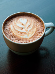 Close up hot cappuccino coffee cup with heart shape latte art on wood table at cafe, tone filter