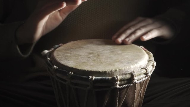 A man finishing playing the djembe drum covered with talcum powder on the dark background, slow motion 4x