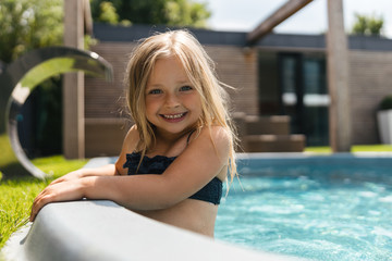 Mirthful girl in swimsuit relaxing in the pool and smiling