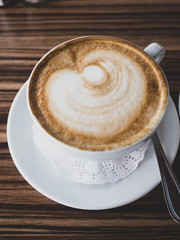 A ceramic cup of latte art coffee on the wooden table