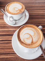 Two cups of cappuccino with latte art on wooden table. Beautiful foam, white ceramic cups, morning coffee