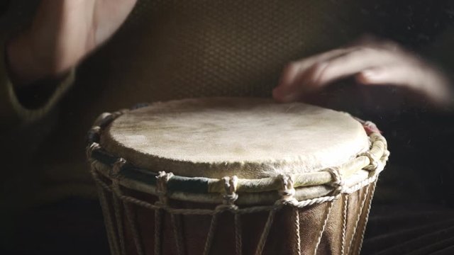 A man playing the djembe drum covered with talcum powder on the dark background, front view