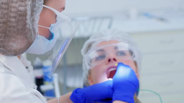 Dentist make fluoridation of teeth after ultrasonic cleaning for young woman. Stomatologist apply fluoride on patient's teeth. Portrait of young woman. Stomatology clinic, cure, treatment, procedure.