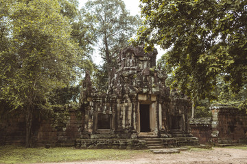 Fototapeta na wymiar A ruined temple made of rustic rocks in Ankgor Thom, Cambodia surrounded and covered by a lot of vegetation - World Heritage by UNESCO in 1992