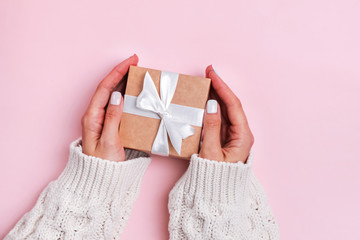 Woman's hands in knitted sweater holding giftbox on the light pink background