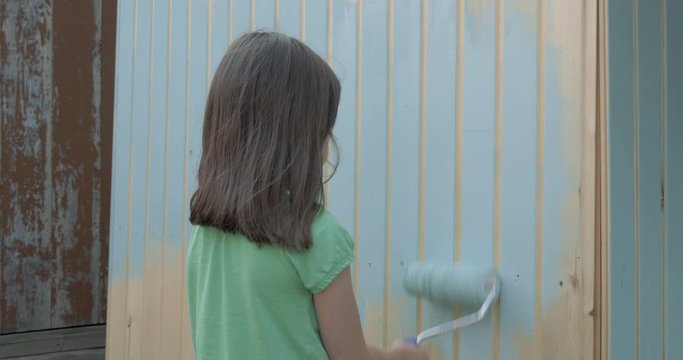 Young girl painting little wooden house with a roller