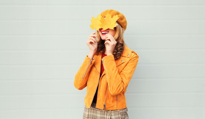 Autumn mood! happy smiling woman holding in her hands yellow maple leaves hiding her eyes over gray...