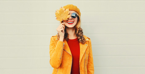 Autumn mood! happy smiling woman holding in her hands yellow maple leaves hiding her eye over gray wall background