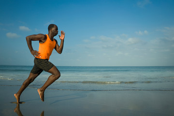 athletic full body portrait of young attractive and fit black afro American man running on the beach doing Summer fitness jogging workout at the sea in healthy lifestyle concept