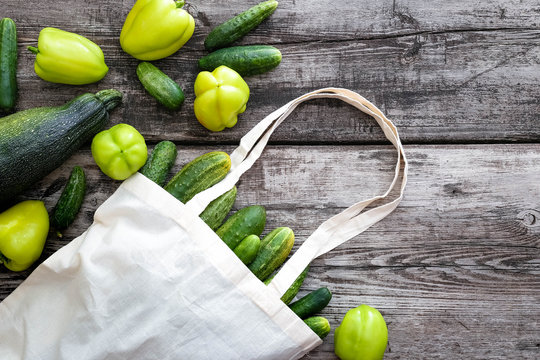 Bag canvas fabric white for mockup blank template on wooden background with vegetebles inside: cucumbers, bell pepper, zukini. Zero waste.Handmade shopping bags,textile glocery bag, multi-use bag.