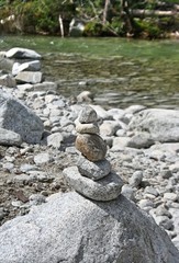 Fototapeta na wymiar Stones in the mountains arranged in a pyramid. Stones stacked on each other in the background of nature, relaxation and meditation. In the background a mountain stream.