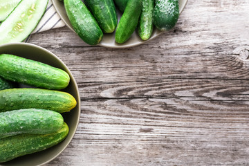 Top view fresh farm cucumbers in rustic plates and chopped cucumber on a towel,  on wooden table, copy space. 