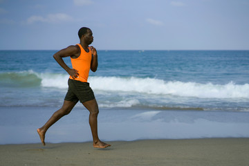 Fototapeta na wymiar athletic full body portrait of young attractive and fit black African American man running on the beach doing Summer fitness jogging workout at the sea in healthy lifestyle