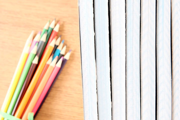 Obraz premium A stack of inverted shared notebooks on a table next to a blurred focus colored pencils. Brown table background.The concept of preparation for school