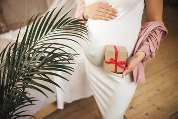 Young pregnant woman holding gift box with red ribbon