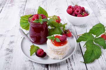 Raspberry jam on pieces of white wheat bread on ceramic plate on white wooden table