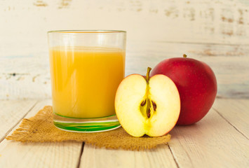Apple juice in a glass and red apple on a white wooden background.