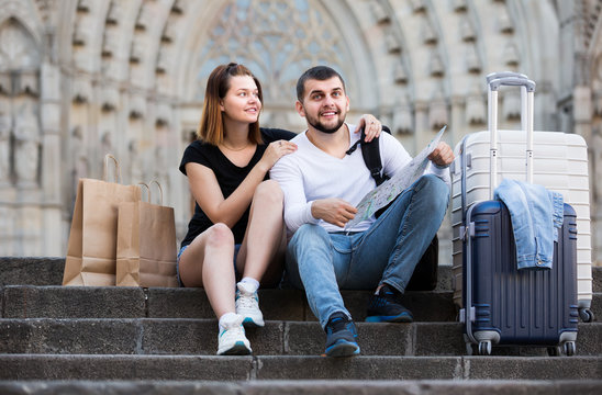 Smiling man and woman sitting at stairs with map