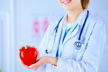Female doctor with stethoscope holding heart, on light background. Health, medicine, people and...