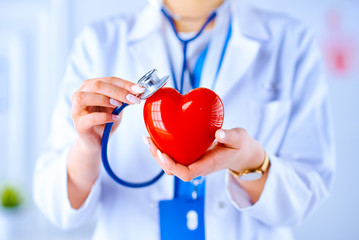 Female doctor with stethoscope examining red heart. Health, medicine, people and cardiology concept