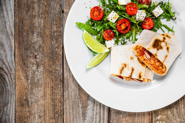 Burrito with vegetable salad on white plate