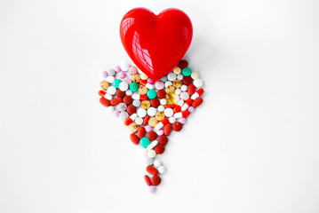 Multicolored pills on a table in the shape of a heart on a white background. Red heart . Doctor's hands on the table near the heart and pills. Top view with copy space. Medicine concept