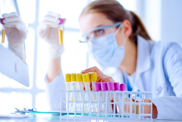 Female scientist explore a test tube with liquid in a laboratory. Researcher is surrounded by medical vials and flasks
