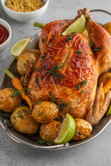 Chicken baked with potatoes, ketchup, lime and herbs in grey pan.