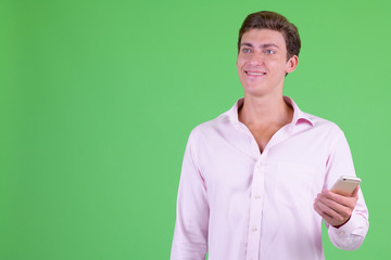 Portrait of young happy businessman thinking while using phone
