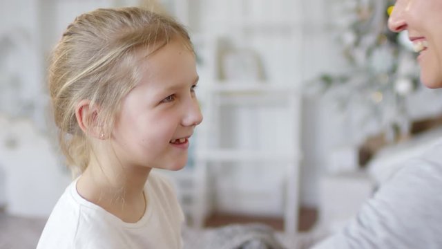 Close up view of smiling little girl hugging mother with love on Christmas Day; defocused fairy lights flickering in the background