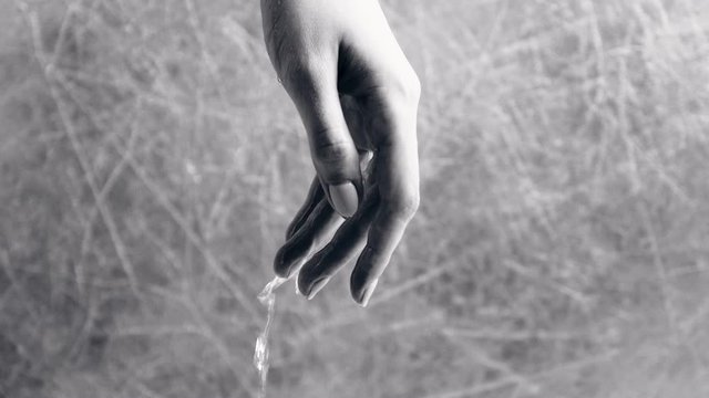 Water flows through the woman's hand on grey background. Time as water flows through the fingers. Hand close-up. Black and white.