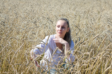 portrait of a beautiful young woman in a white blouse with long blond hair in a field of golden wheat ears on a summer day