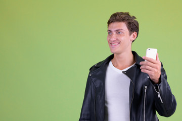 Portrait of young happy rebellious man thinking while using phone