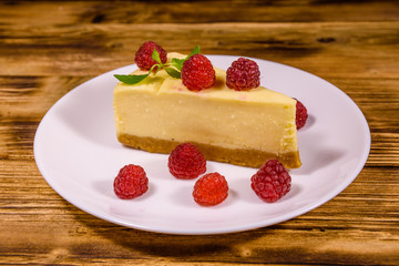 White plate with cheesecake New York, leaf of mint and raspberries on wooden table