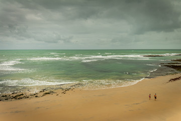 Beautiful view of the marine coast. Sea water with white foam waves. Couple walking on the cloudy beach.