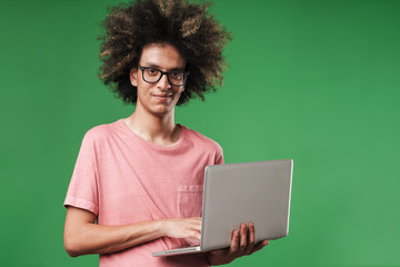 Smiling happy curly guy posing isolated over green wall background using laptop computer.