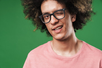 Young curly guy posing isolated over green wall background winking to you.