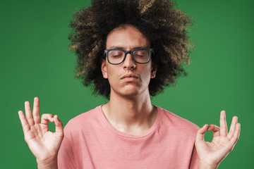Concentrated curly guy posing isolated over green wall background meditate.