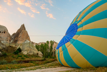 Obraz premium Big balloon on the ground. Preparing for the flight. A unique rocky area at dawn with pink tender clouds. Cappadocia Turkey.