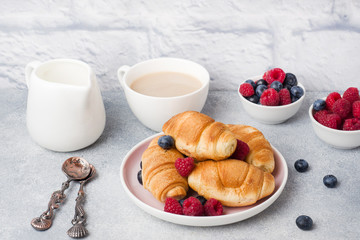Croissants with fresh raspberries and blueberries on grey concrete background. Copy space. concept of Breakfast coffee honey