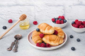 Croissants with fresh raspberries and blueberries on grey concrete background. Copy space. concept of Breakfast coffee honey
