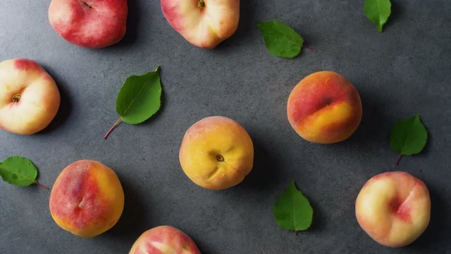 Nice yummy fresh peaches with green tree leaves on dark texture surface. Top view. Summer fruits. 4k.