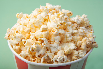 Top view of striped paper cup with popcorn on green background. Snack for a movie. Close-up.