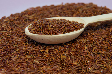 Unpolished red rice in wooden spoon. Long grain red rice, rice background. Red rice.