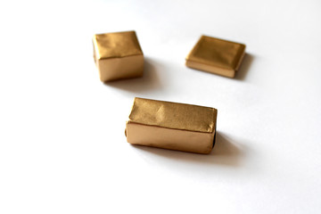 Chocolate candies wrapped in golden foil isolated on white surface. Template for greeting card, poster or invitation. Sweets scattered on white smooth table. Backdrop or background